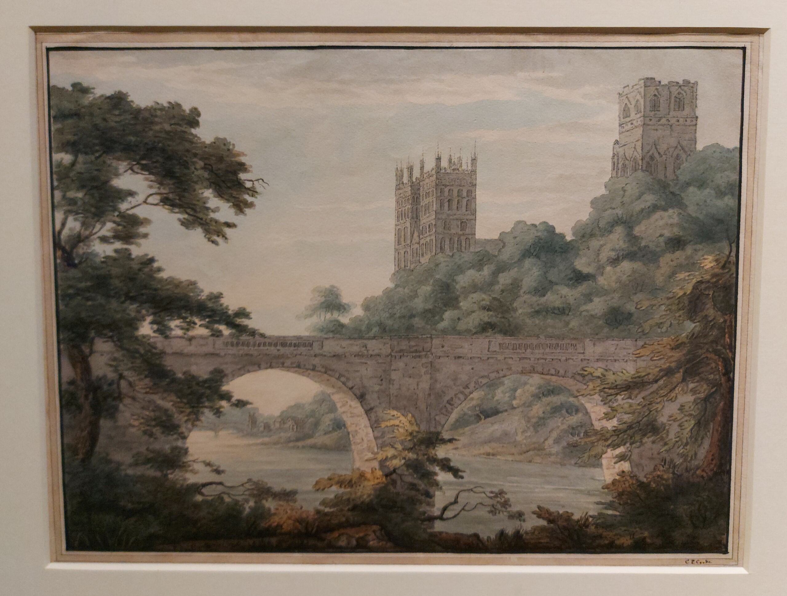 A full-size photograph of a landscape painting depicting Prebends Bridge and Durham Cathedral in Durham City. The river runs through the middle of the artwork, with trees and other shrubbery flanking both sides.