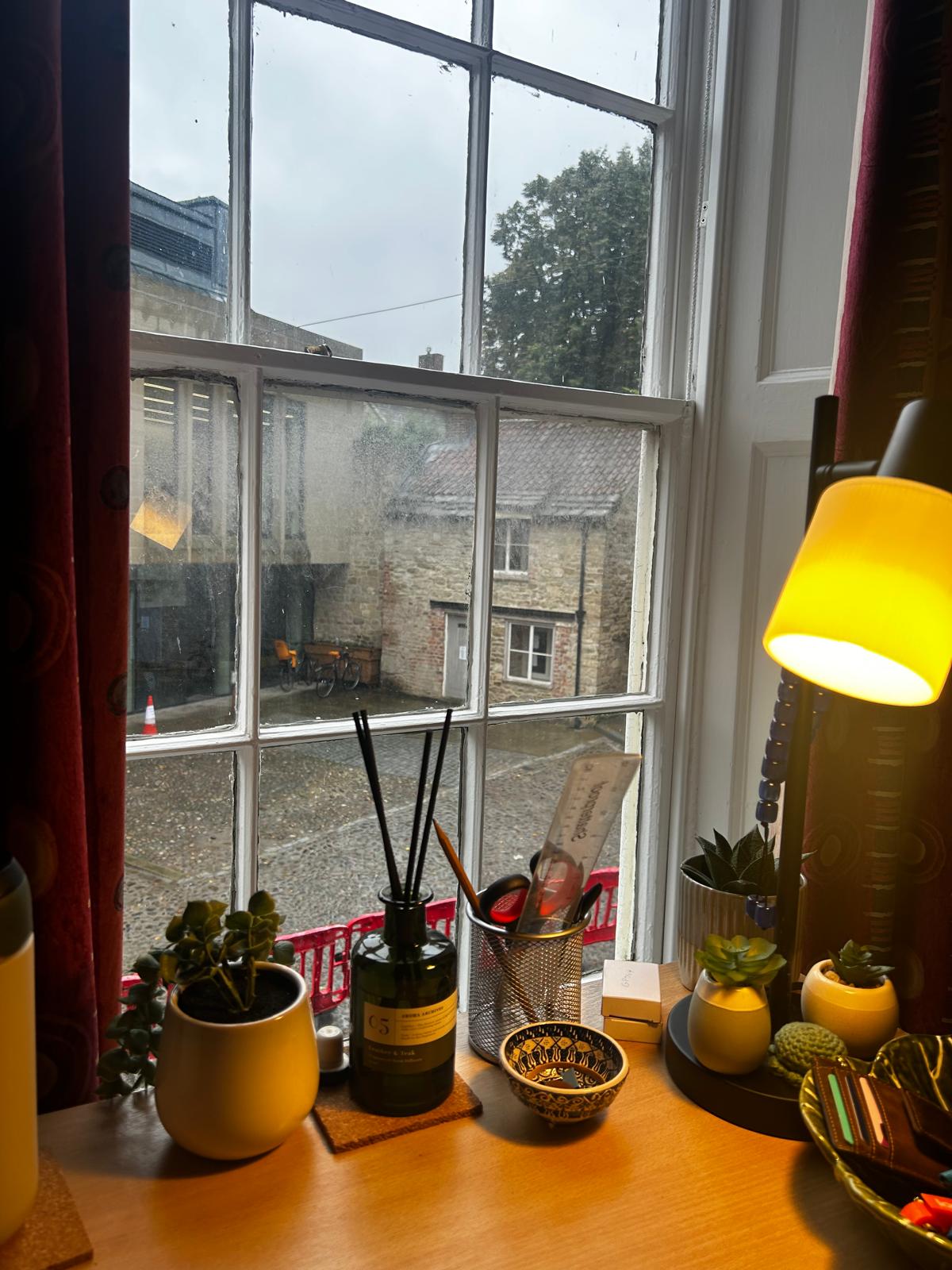 A photograph of a desk, with a lamp and other assorted items, overlooking the Bailey in Durham, with St John's LRC in the background.