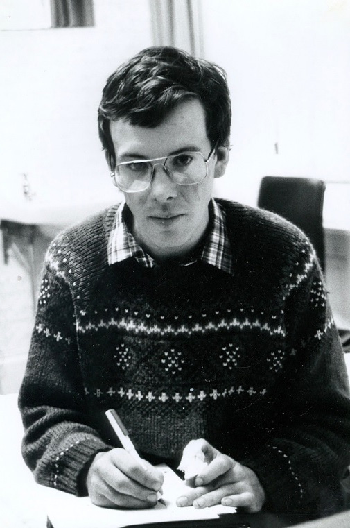 A young man sits writing with a mostly eaten apple in his hand