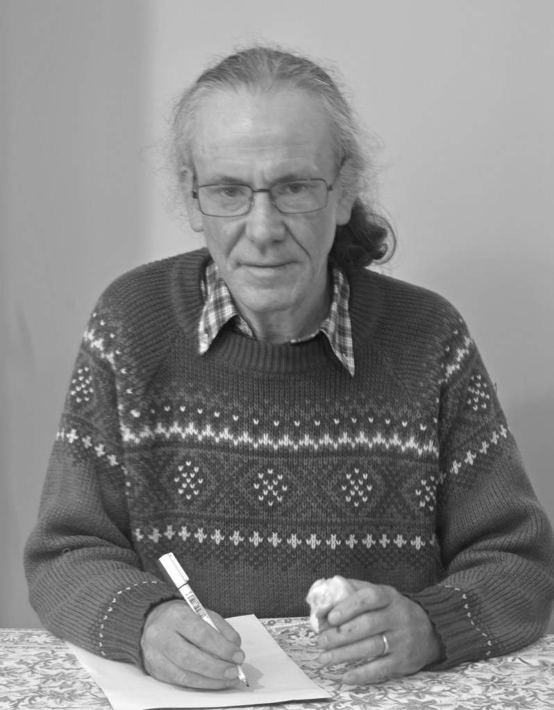 A man sits writing with a mostly eaten apple in his hand